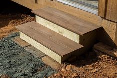 two wooden steps leading up to the side of a building with dirt on the ground