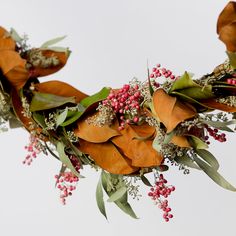 a bunch of flowers that are on top of a branch with leaves and red berries