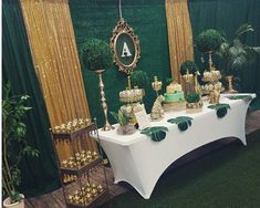 a table topped with lots of cakes and cupcakes next to green wallpaper