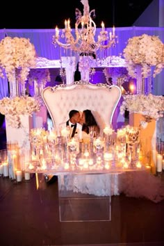 a bride and groom kissing in front of an elaborate chair with candles on it at their wedding reception