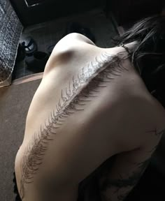 the back of a woman's body with a tattoo on her left shoulder and an intricate fern