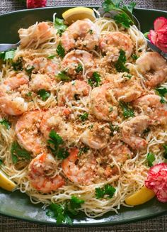 pasta with shrimp and parsley on a green plate next to lemon wedges, garnished with parsley