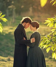 a man and woman standing next to each other under a tree in the sun light