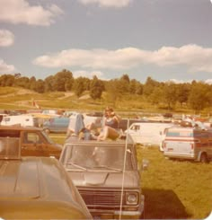 several cars parked in a field with people sitting on the hoods and looking at them