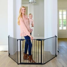 a woman holding a baby in her arms standing next to a black metal gate that is open