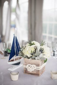 a wooden box filled with white flowers and greenery on top of a table next to cups