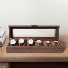 a wooden box with six watches in it on a table next to a stack of books