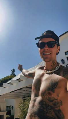 a shirtless man with tattoos on his arm and chest standing in front of a house