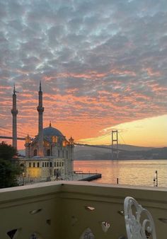 the sun is setting over some water and a building with a bridge in the background