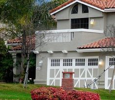 a gray house with white garage doors and red roof tiles on the side of it