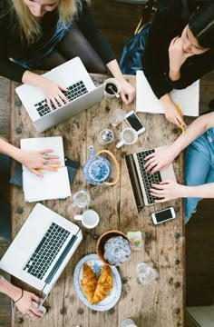 four people sitting at a table working on laptops