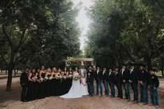 a large group of people standing in front of some trees and bushes at a wedding