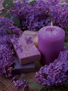 purple candles and soaps are arranged in a wreath with lilacs on the table