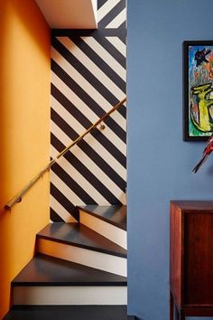 a painting hangs on the wall next to a stair case with a lamp and table