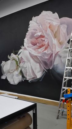 a large pink rose is being painted on the wall in an art studio with ladders