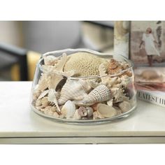 a glass bowl filled with seashells on top of a table next to a book