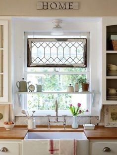 a kitchen sink under a window next to a shelf with dishes and cups on it