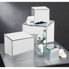 three mirrored cubes with flowers in them on a table next to a mirror box