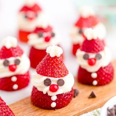 some strawberries with santa hats on them are sitting on a board and ready to be eaten