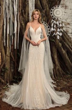 a woman standing in front of a tree wearing a white wedding dress with long veil