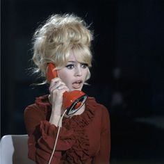 a woman talking on an orange phone while sitting at a table with a white chair