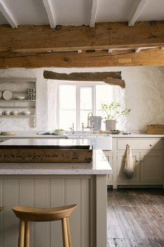 a kitchen with white cabinets and wooden beams on the ceiling, along with two stools