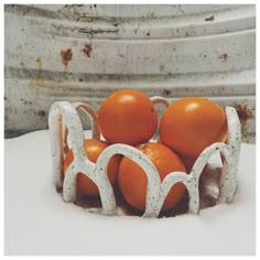 oranges are in a white bowl on top of snow covered ground with rusted metal