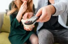 a man holding a remote control next to a woman sitting on a green couch in front of a window