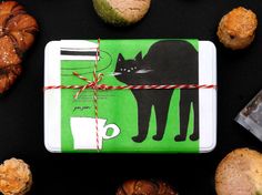 a package wrapped in green paper with a black cat on it next to various pastries