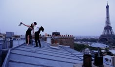 two people standing on the roof of a building in front of the eiffel tower