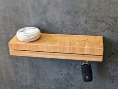 a wooden shelf with a small white bowl on top and a black car key hanging from it