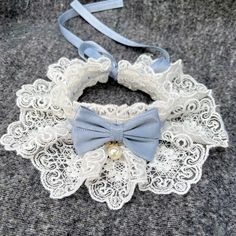 a white lace collar with a blue bow tie on top of grey fabric and a light blue ribbon