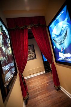 two televisions mounted to the side of a wall next to red curtained drapes