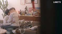 two people sitting on a couch in a living room next to a zebra stuffed animal