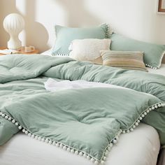 an unmade bed with green sheets and pillows