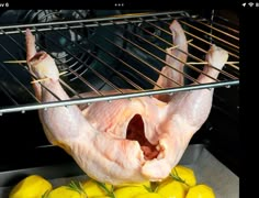 raw chicken in an oven with lemons on the side and rack above it that has been cooked