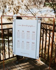 a wedding seating plan hanging on a wooden fence with trees in the backgroud