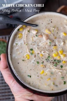 a person holding a bowl of soup with corn on the cob