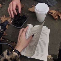 a person is reading a book while holding a cup of coffee and some blackberries