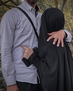 a man and woman standing next to each other in front of trees with their arms around each other