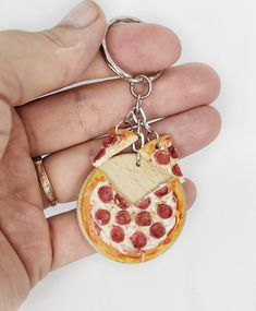 a hand holding a keychain with a slice of pizza on it's side