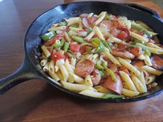 a skillet filled with pasta and sausages on top of a wooden countertop