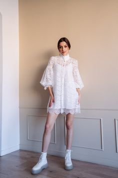 a woman is standing in front of a wall wearing white shoes and a lacy dress