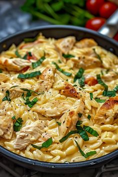 a skillet filled with pasta and chicken on top of a table next to tomatoes