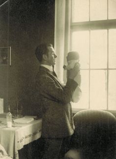 an old black and white photo of a man holding a baby in front of a window