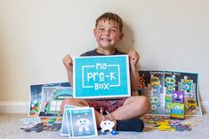 a young boy sitting on the floor holding up a sign that says my pre - k box