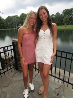 two young women standing next to each other on a stone walkway near a body of water