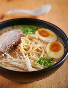 a bowl of ramen with meat, noodles and boiled egg on the side sitting on a wooden table