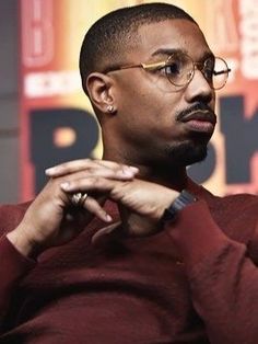 a man with glasses sitting in front of a microphone and looking off to the side