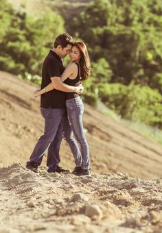 a man and woman standing on top of a hill hugging with trees in the background